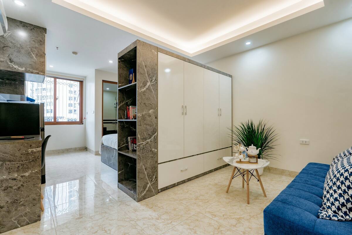 A modern living room with a blue sofa, a marble fireplace, a white wardrobe, and a small table with a plant.
