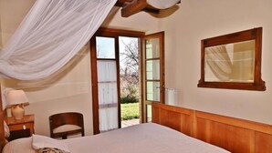 Une chambre à coucher comprenant un lit, une table de chevet, une chaise, une fenêtre avec des rideaux et une tête de lit en bois.