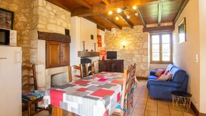 A cozy dining area with a wooden table and chairs, a stone wall, and a blue sofa in a rustic setting. - House in Dordogne Valley, pets allowed (Cénac-et-Saint-Julien)