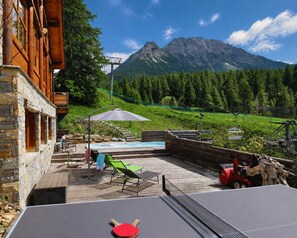A wooden deck with outdoor seating, a pool, and a mountain view.