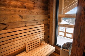 A wooden cabin interior with a bench and a window overlooking a snowy landscape.