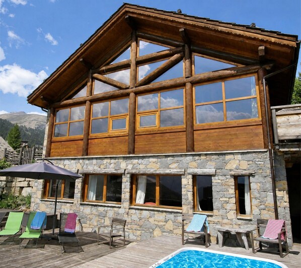 A two-story wooden building with stone walls and a pool area with lounge chairs.
