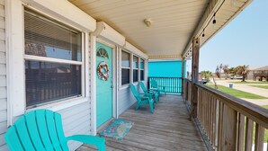 A covered porch with turquoise chairs and a teal door, featuring a wooden railing and a view of the surrounding area. - PC635 Close to Beach and Restaurants, Golf Cart Access (Port Aransas)