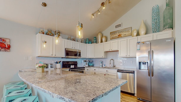 A kitchen with white cabinets, a granite island, and a stainless steel refrigerator. - PC635 Close to Beach and Restaurants, Golf Cart Access (Port Aransas)