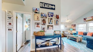 A living room with a blue sofa, a coffee table, and a wall decorated with various framed photos. - PC635 Close to Beach and Restaurants, Golf Cart Access (Port Aransas)