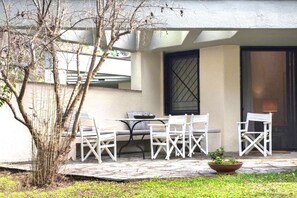 Relax in a serene outdoor space with a table and chairs, surrounded by lush greenery and a charming tree.