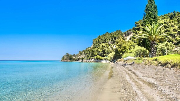 A beach with clear turquoise water, pebbly shore, and lush greenery. - Seafront Paradise Home (Skala Fourkas, Halkidiki)