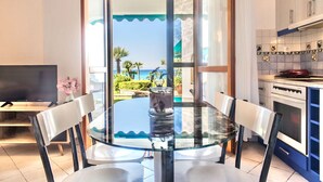 A dining area with a glass table and chairs, a TV, and a view of the sea through a glass door. - Seafront Paradise Home (Skala Fourkas, Halkidiki)