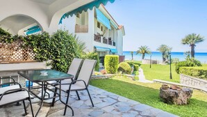 A patio with a glass table and chairs, a stone pathway, and a view of the sea. - Seafront Paradise Home (Skala Fourkas, Halkidiki)