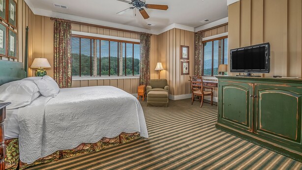 A hotel room with a bed, a desk, a television, and a ceiling fan.