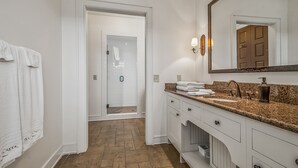 A modern bathroom with a granite countertop, a large mirror, and a walk-in shower.
