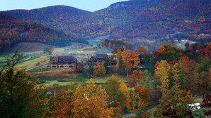Ein großes, mehrstöckiges Gebäude mit Steinaußenseite, eingebettet in ein Tal, umgeben von herbstlich gefärbten Bäumen.