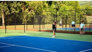 Guests can enjoy a game of tennis on this outdoor court surrounded by trees.