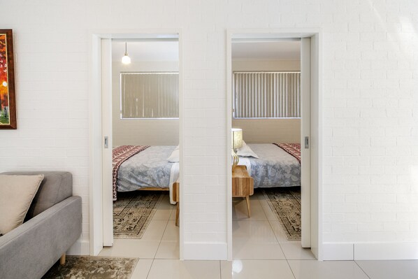 A room with a bed, a nightstand, a lamp, and a grey sofa.