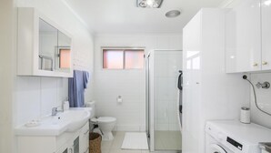 A modern bathroom with a sink, toilet, shower, and a washing machine.