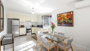 A modern kitchen with white cabinets, a stainless steel refrigerator, and a dining area with a glass table and chairs.