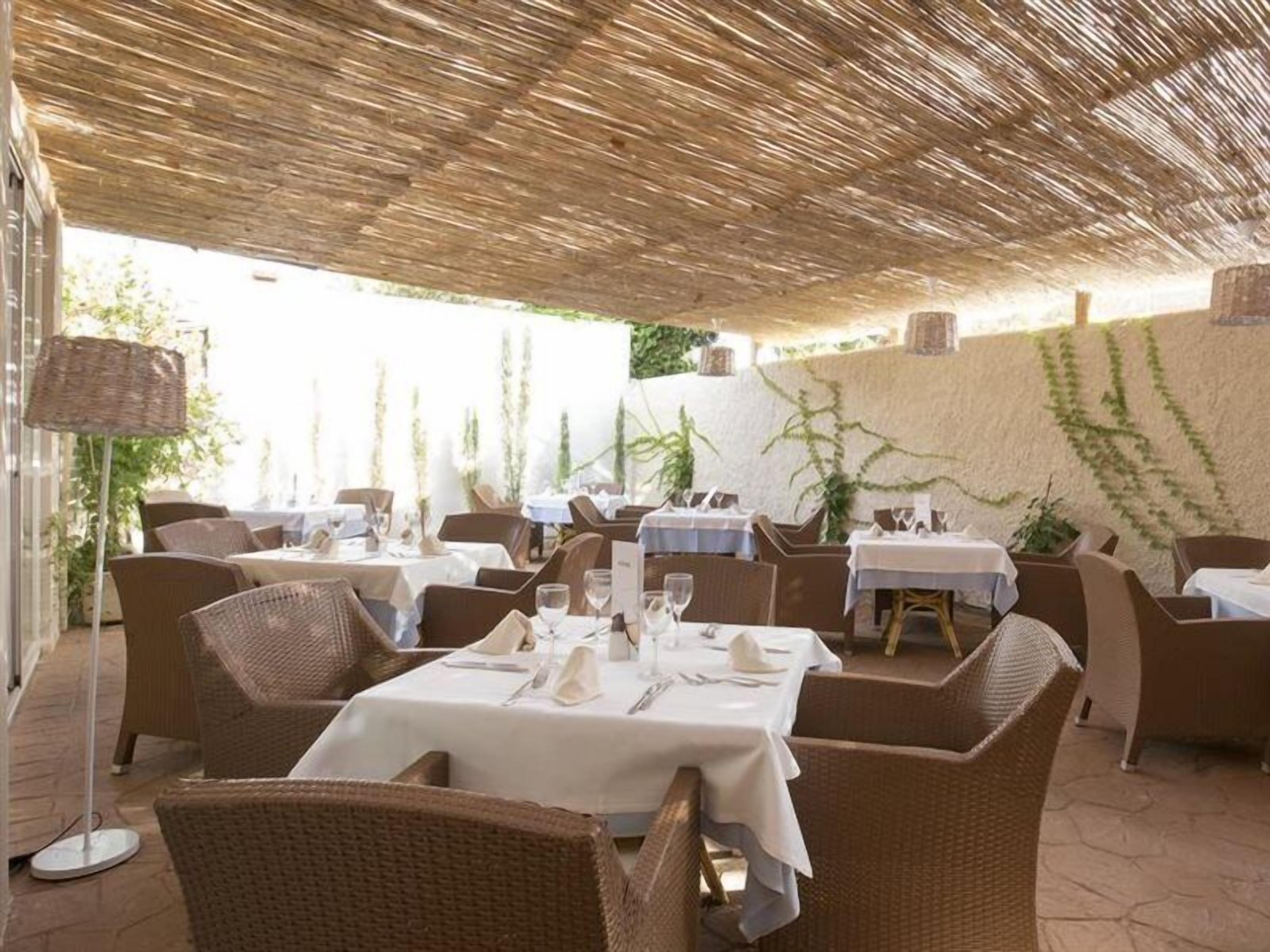 Un área de comedor al aire libre con mobiliario de mimbre, manteles blancos y un techo de paja.