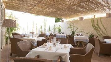 Un área de comedor al aire libre con mobiliario de mimbre, manteles blancos y un techo de paja.
