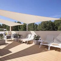 Un espacio de estar al aire libre cubierto con sillas reclinables blancas y una mesa, rodeado por una terraza de madera y un dosel grande.