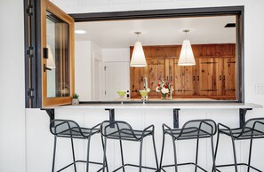 A kitchen with wooden cabinets, a white countertop, and a large mirror. There are two hanging pendant lights, a sink, and a vase with flowers.