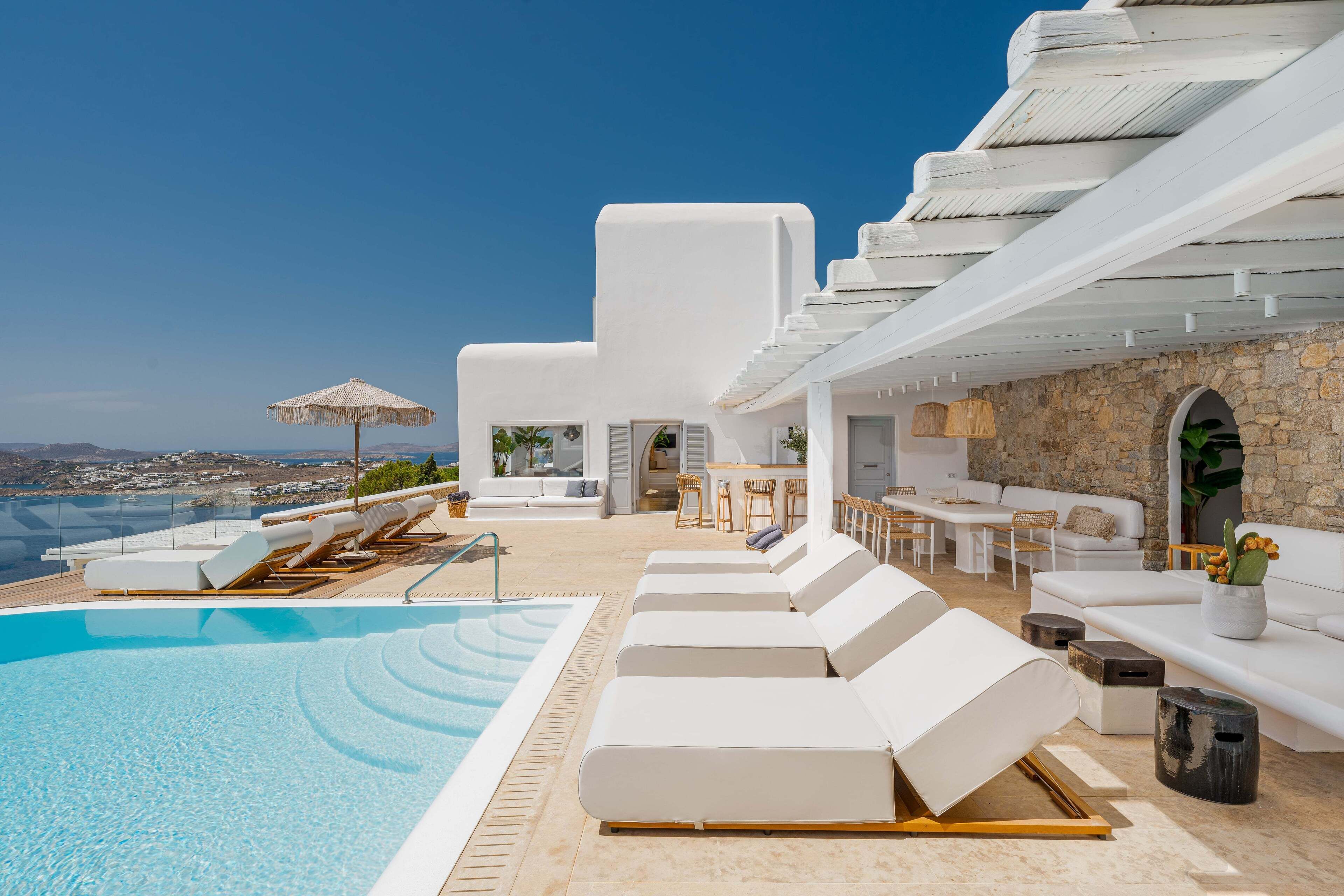 A poolside area with lounge chairs, a dining table, and a view of the sea.