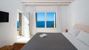 Une chambre avec un grand lit, une vue sur la mer et un mur en pierre.