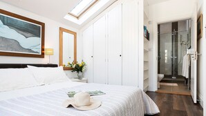A bedroom with a large bed, a skylight, a closet, and a bathroom with a glass door.