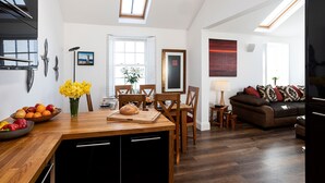 A modern kitchen with a wooden island, dining area with chairs, a sofa, and a TV.