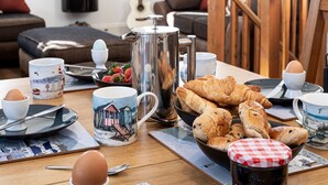 A breakfast setting with a coffee pot, croissants, and jam on a wooden table.