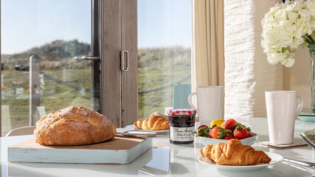 Una mesa de desayuno con croissants, un tarro de mermelada, fresas y un jarrón con flores.