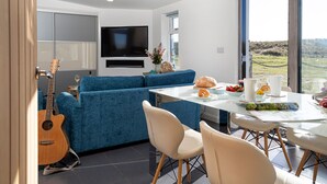Una sala de estar moderna con un sofá azul, una mesa de comedor con sillas, una guitarra y un televisor montado en la pared.