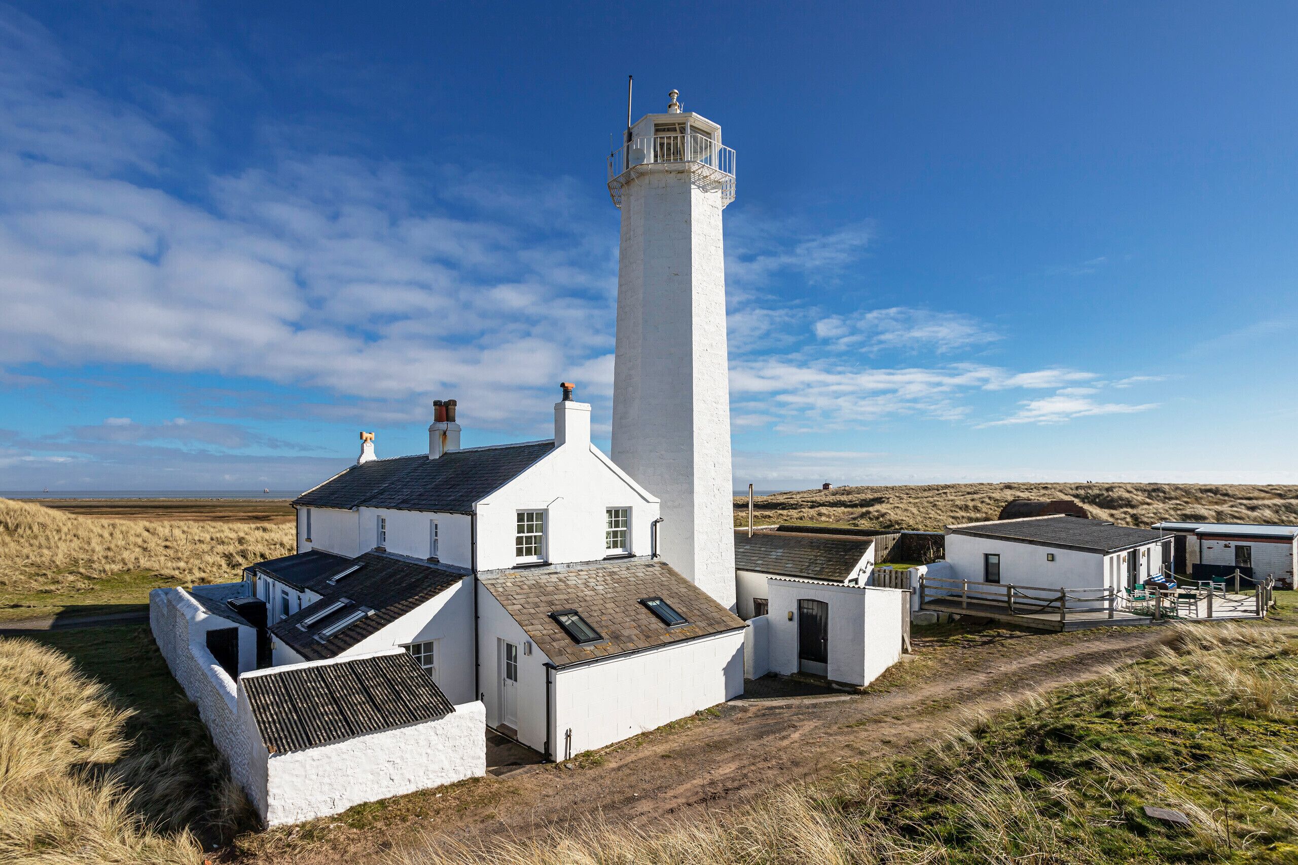 A white lighthouse with a tall tower and a shorter building attached to its base.