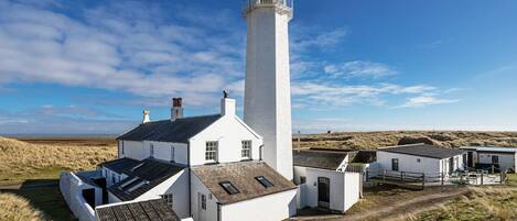A white lighthouse with a tall tower and a shorter building attached to its base.