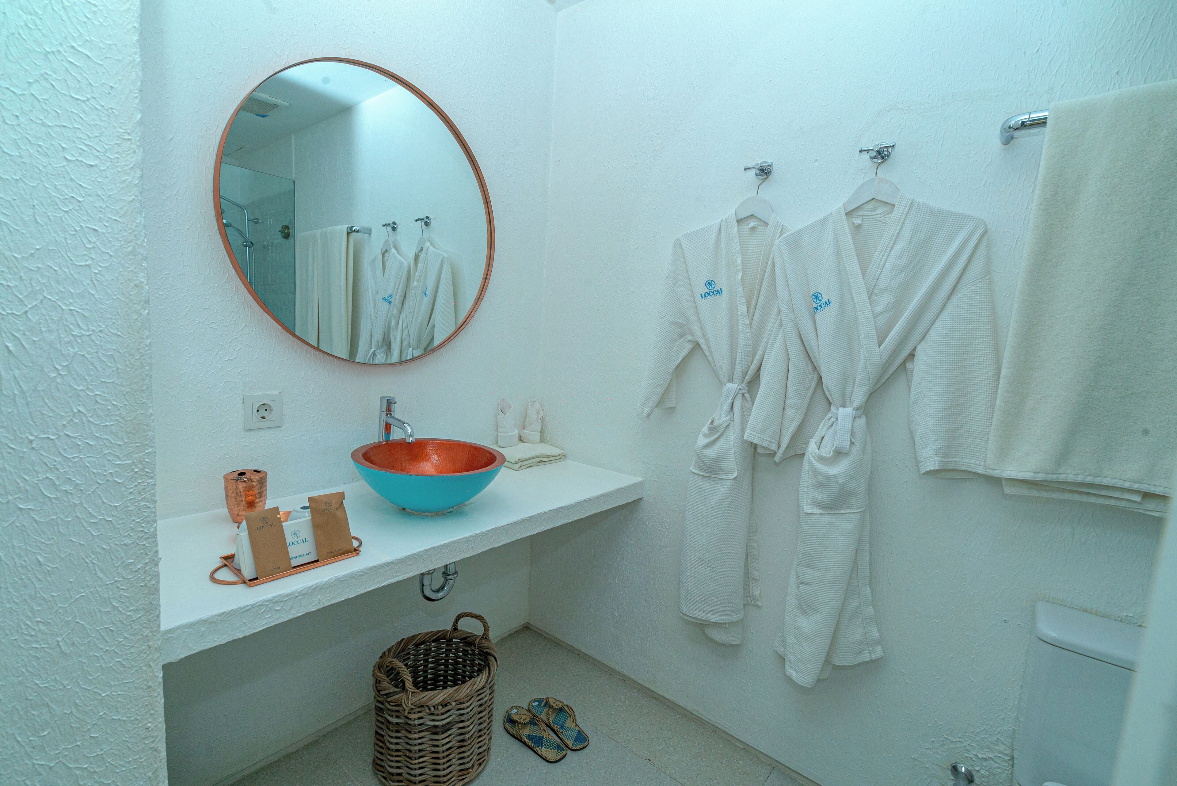 A bathroom with a round mirror, white sink, and two white robes hanging on hooks.