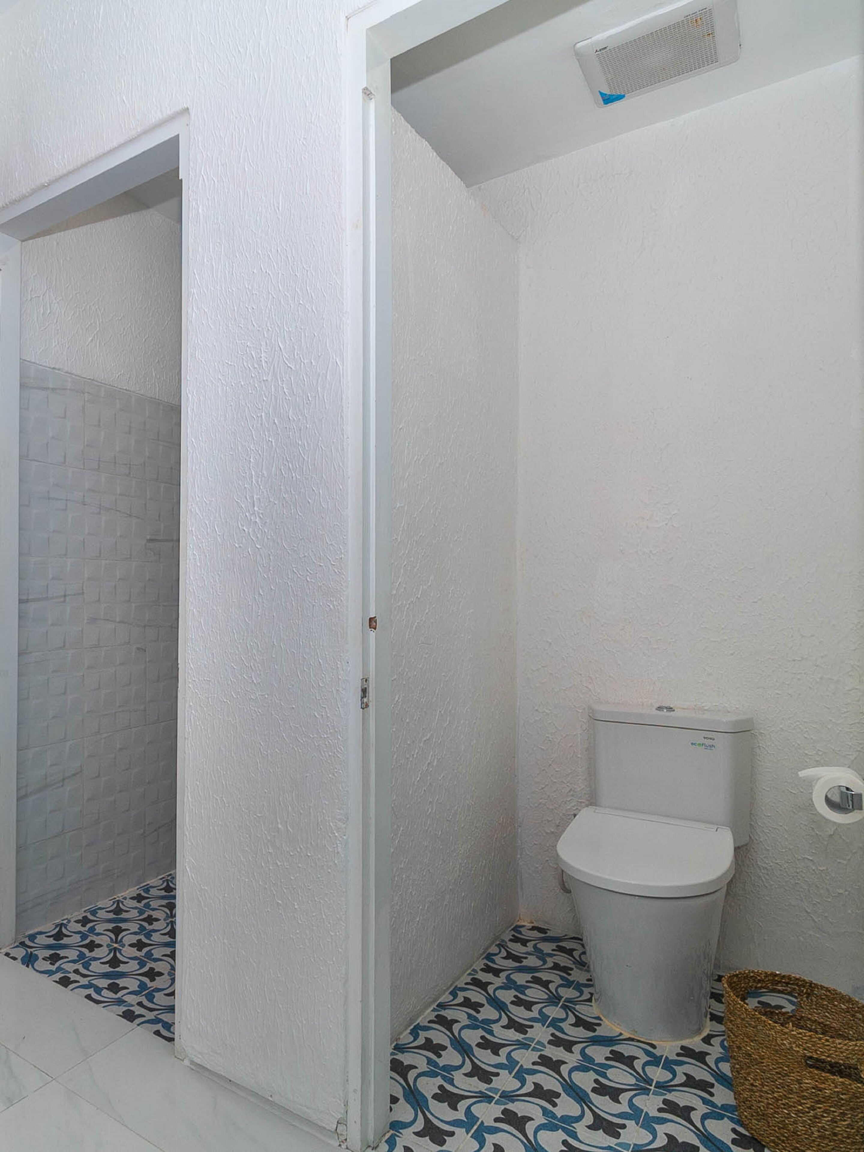 A bathroom with a white toilet, a shower area with a white door, and patterned floor tiles.