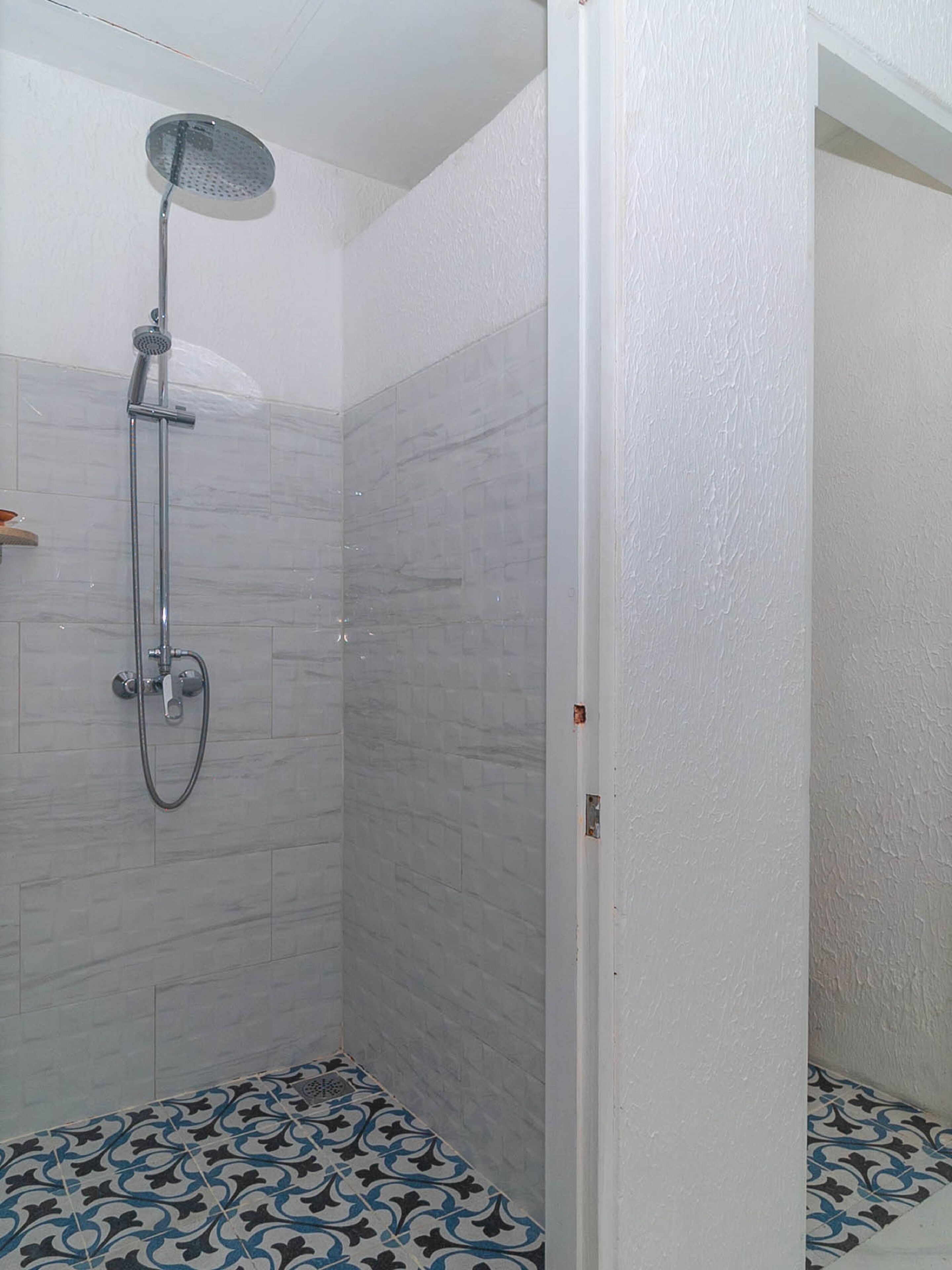 A shower with a handheld showerhead and a wall-mounted faucet. The shower has a tiled floor with a blue and white pattern.