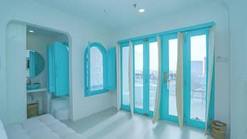 A room with a white sofa, a large window with teal curtains, and a view of the outside.