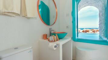 A bathroom with a white sink, a round mirror, and a view of the sea through a turquoise arch window.