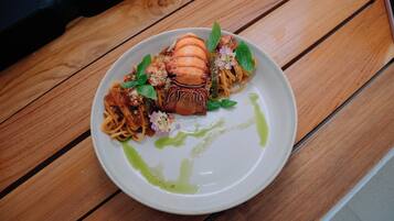 A plate of pasta with a lobster tail, garnished with basil and flowers, on a wooden table.