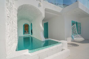 Un edificio de paredes blancas con piscina, puertas turquesa y una silla colgante.