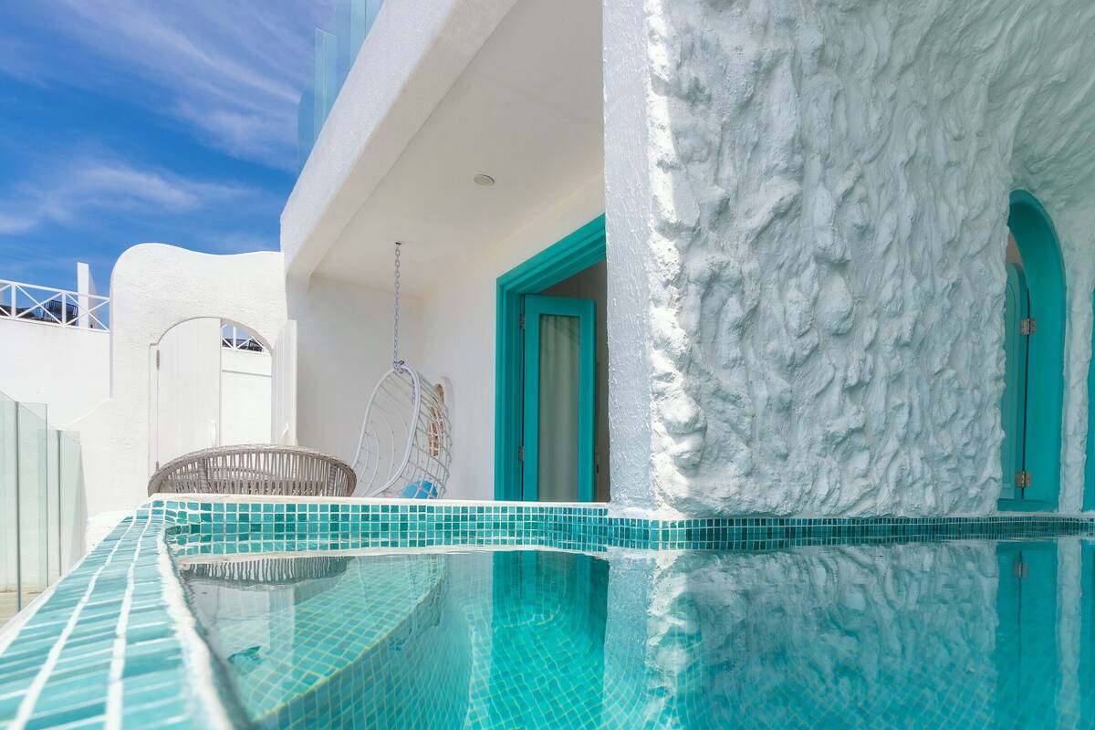 A pool area with a white textured wall, turquoise doors, and a hanging chair.