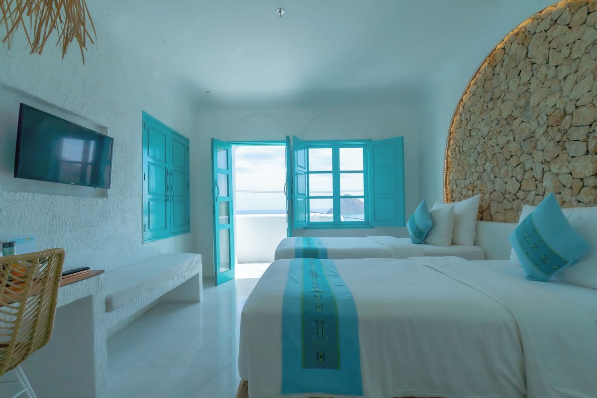 A bedroom with two beds, a TV, a desk, and a view of the beach.