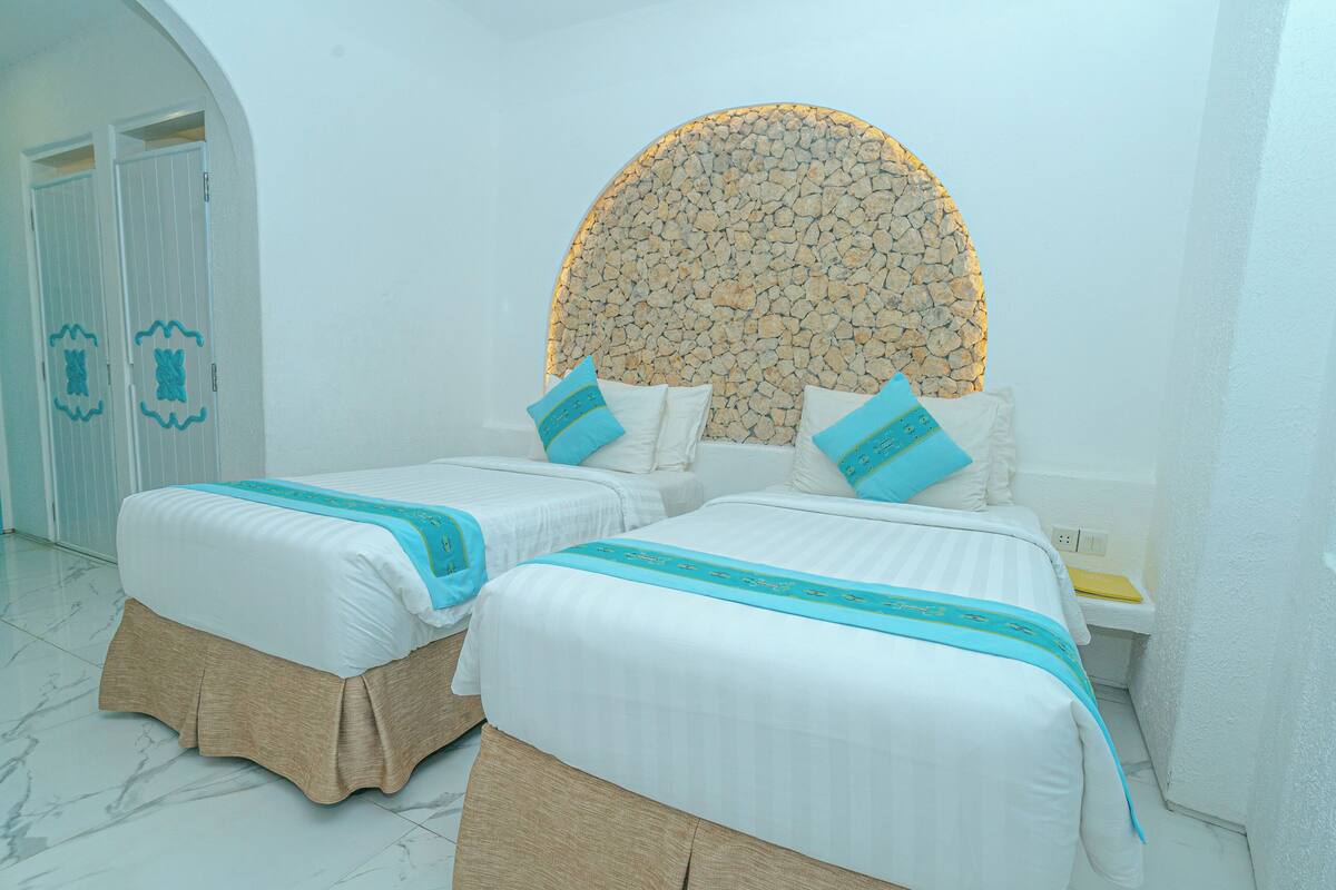 A hotel room with two beds, a stone wall headboard, and a white door with decorative elements.