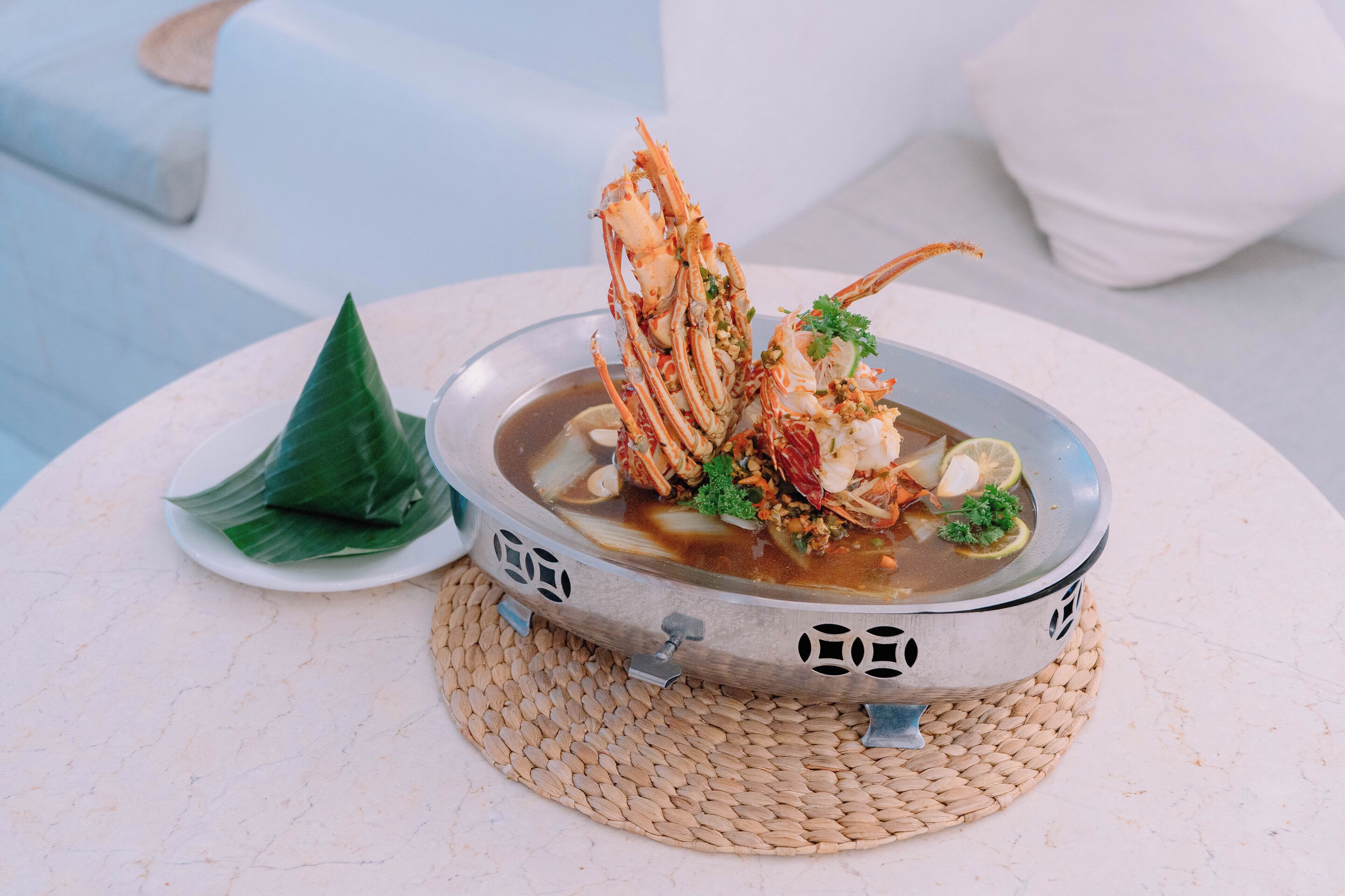Un plato de mariscos sobre un tapete tejido, un plato blanco con una hoja y una silla moderna al fondo.