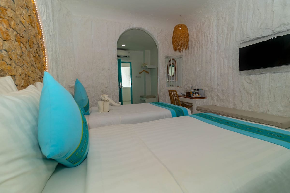 A hotel room with two beds, a desk, a chair, a TV, and a bathroom visible through an archway.