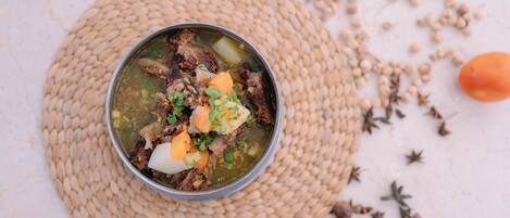 Un tazón de sopa con carne y verduras sobre una estera tejida.
