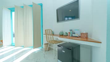 A room with a desk, a chair, a television, a refrigerator, and a window with curtains.