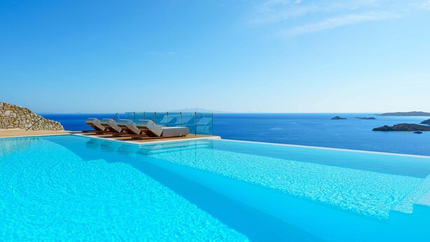 Piscina infinita azul y cristalina con sillas de descanso y vista al océano.