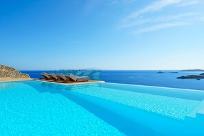 A clear blue infinity pool with lounge chairs and a view of the ocean. - Eternity (Mykonos)