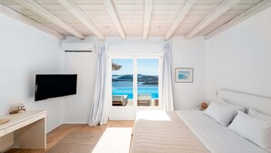 Un dormitorio con cama, escritorio, televisión y vista al mar a través de un ventanal.